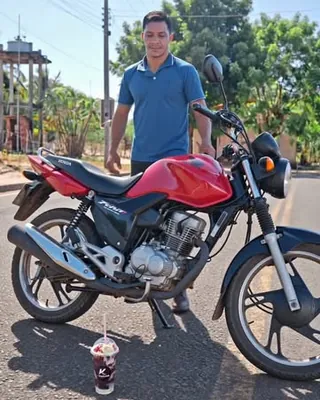 Entregador da Keprovar em pé ao lado da moto vermelha, com um copo de açaí no chão da rua